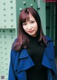 A woman in a blue coat standing in front of a green wall.